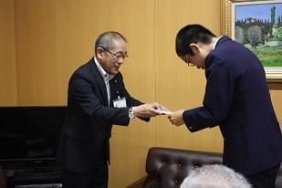 黒いスーツを着た男性が青いスーツを着た男性に、何かを渡している写真