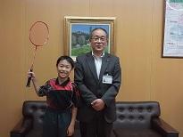 右から、スーツを着た男性と、バドミントンラケットを右手で掲げている男子生徒が並んでいる写真