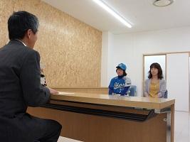 スーツを着た男性と机を挟んで、ユニフォームを着た女子生徒と、女性が椅子に座っている画像