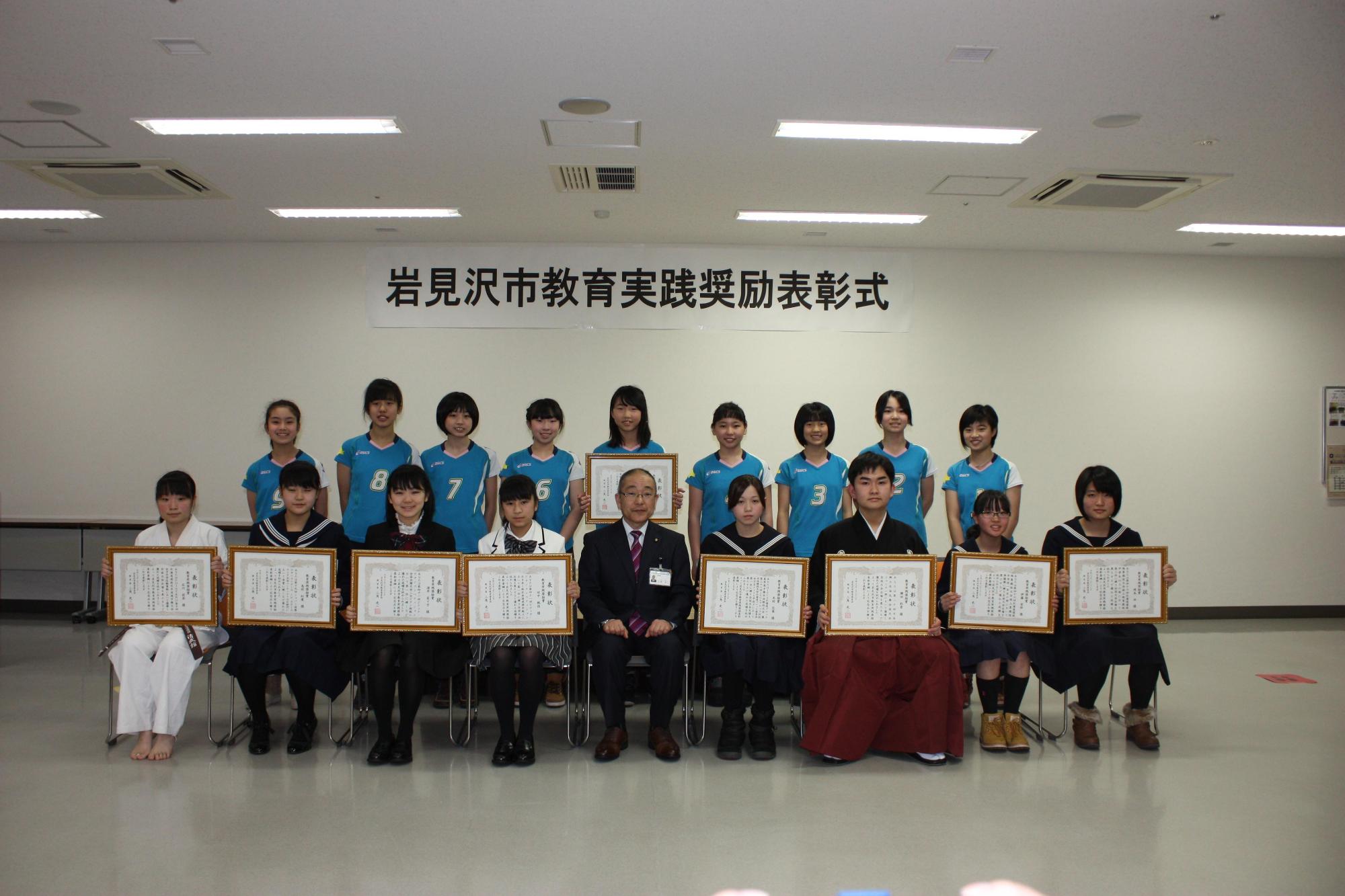 受賞者18名の書状を手にして空手着やユニフォームや制服などで座っている写真