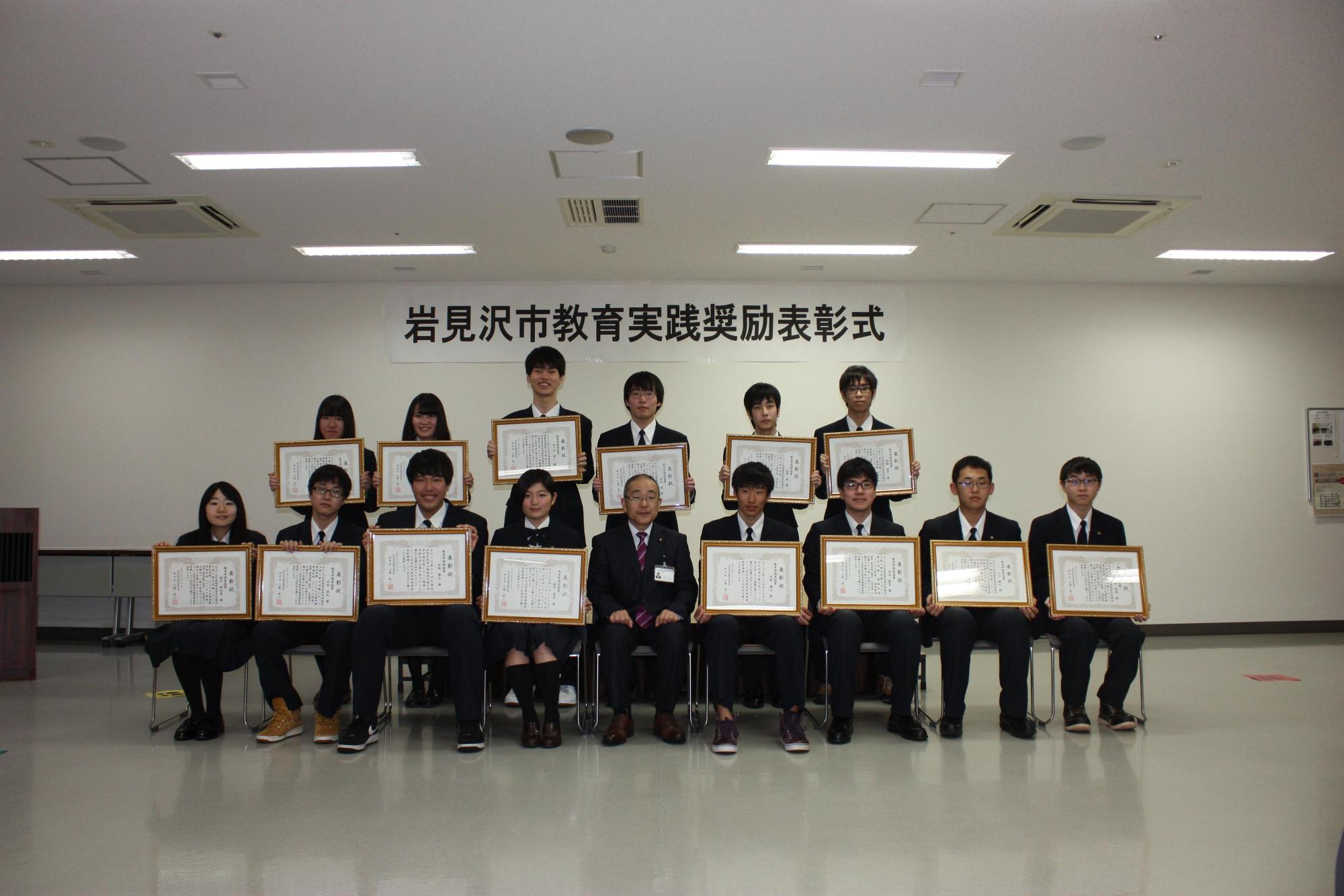 賞状を持つ14名の受賞者たちと前列の真ん中に何も持っていない人が座っている写真