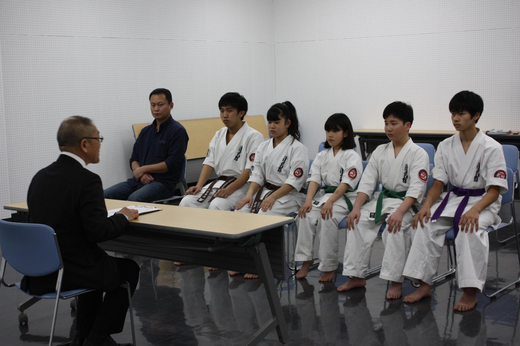 空手大会に出場する柔道着の学生たちと教育長が対面して座る写真