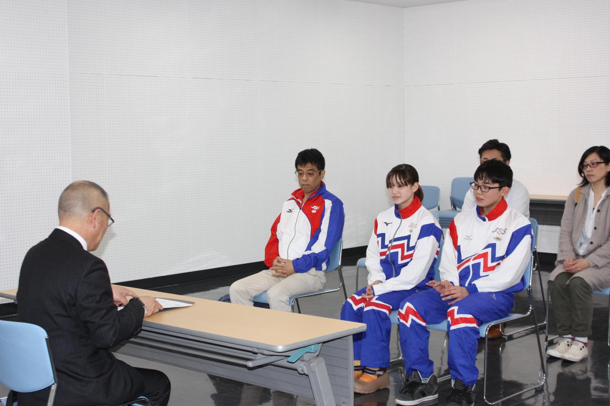 水泳全国大会に出場する学生たちと教育長が対面して座る写真