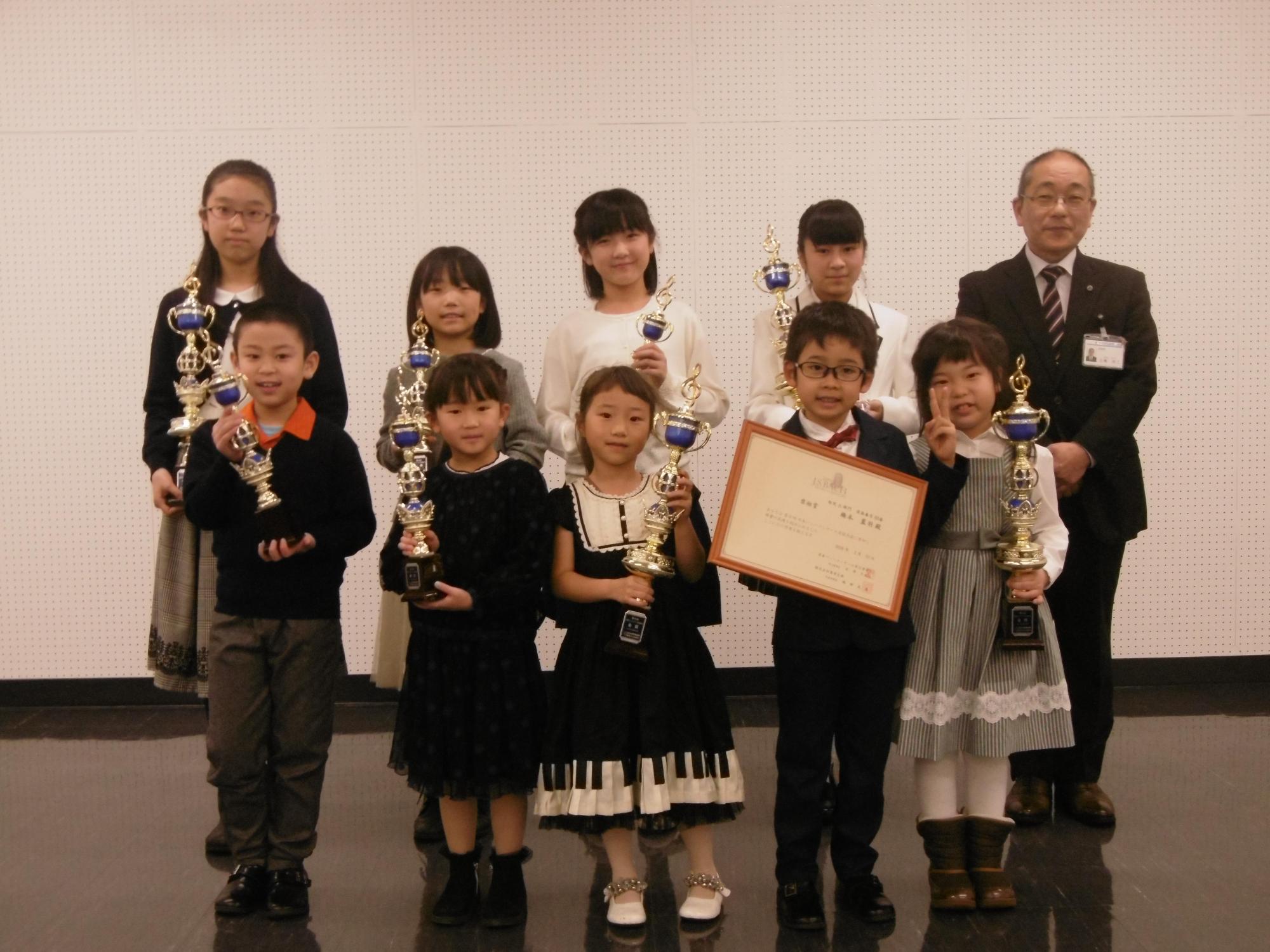 日本バッハコンクールに出場しトロフィーと賞状を持った子どもたちと教育長の集合写真