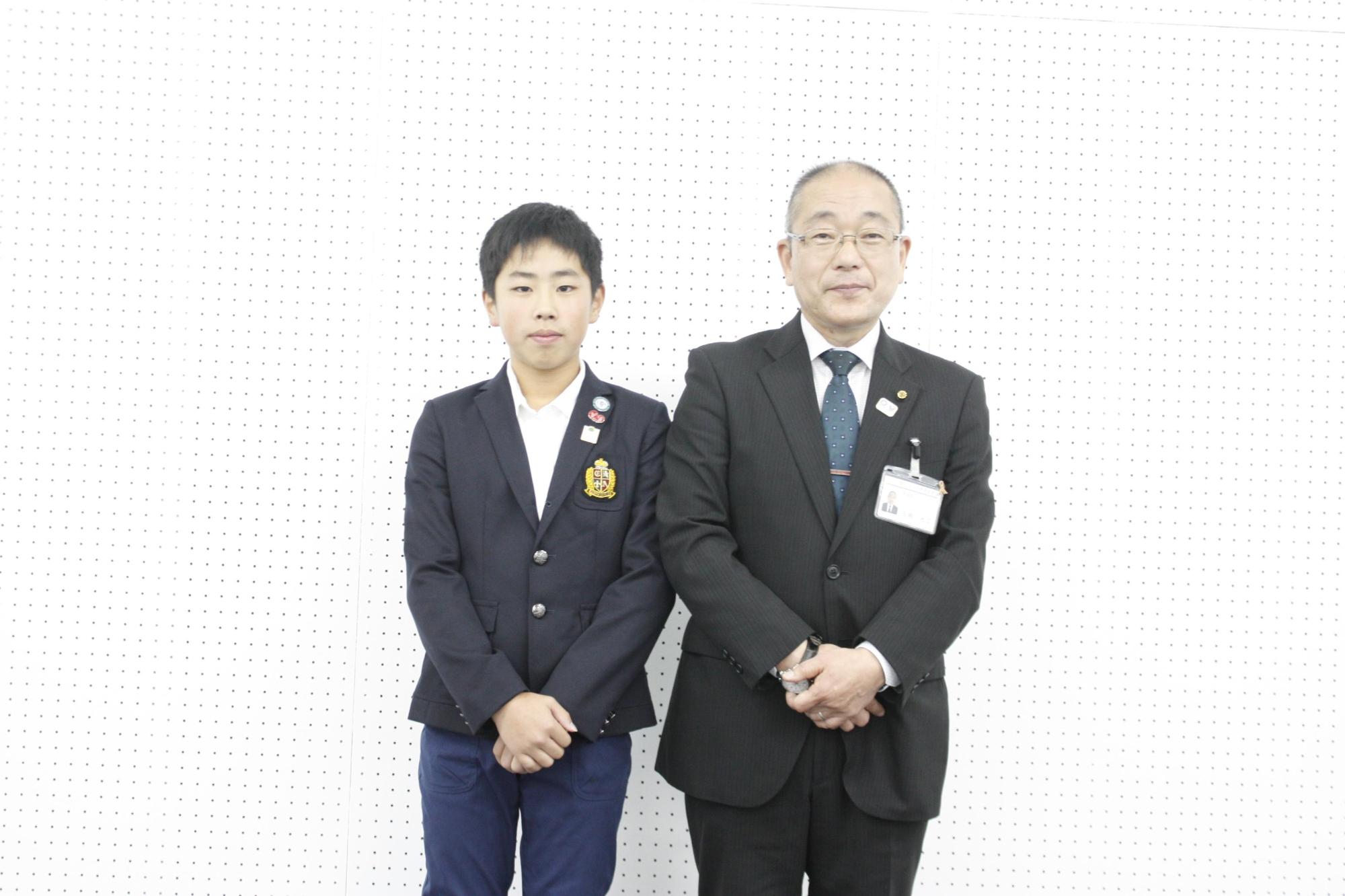 白壁に囲まれた室内で市長と制服の小学生が並んで撮影されている写真