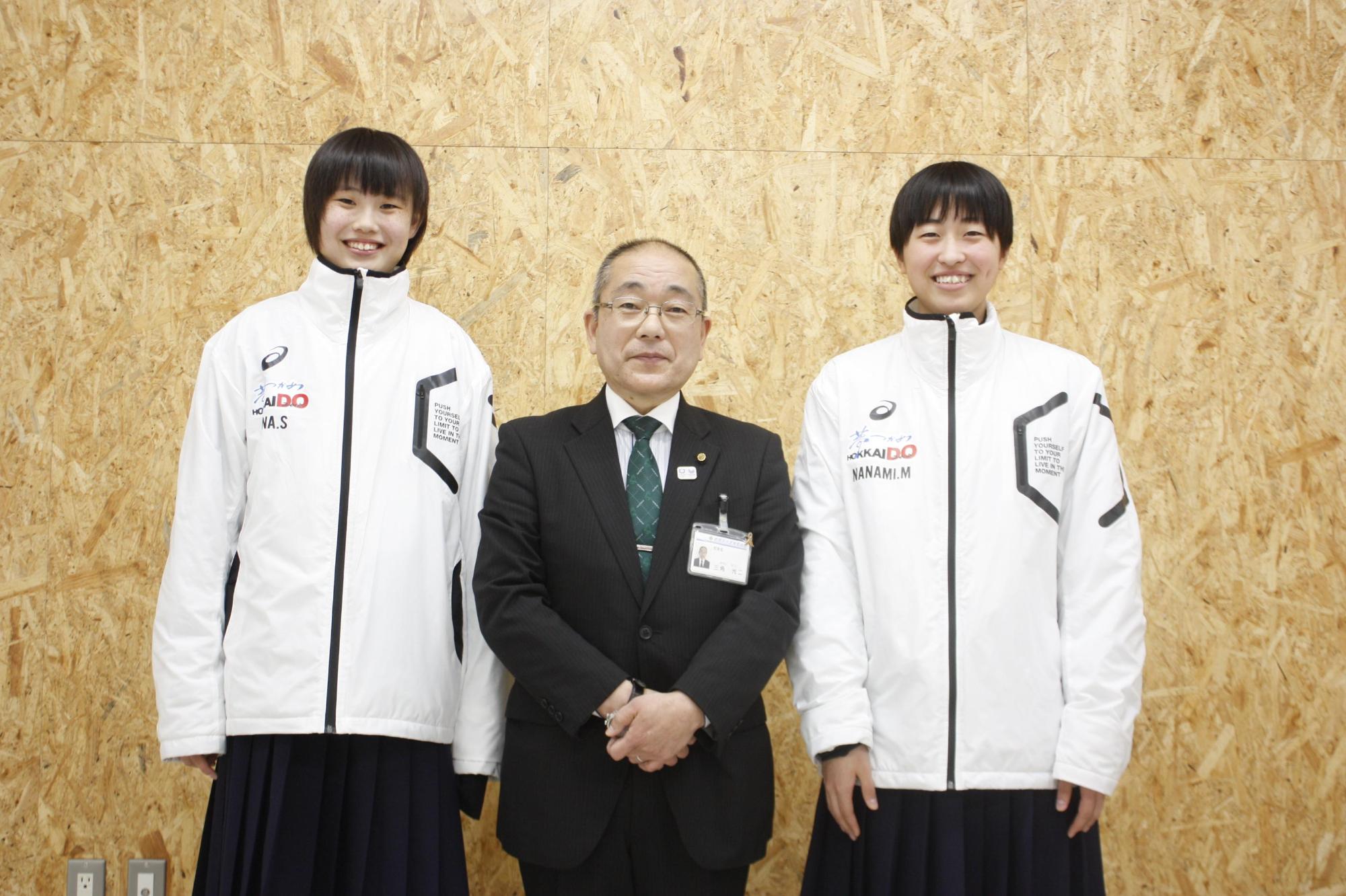 チームのウインドブレーカーを着て教育長と並ぶ女子中学生2人の写真