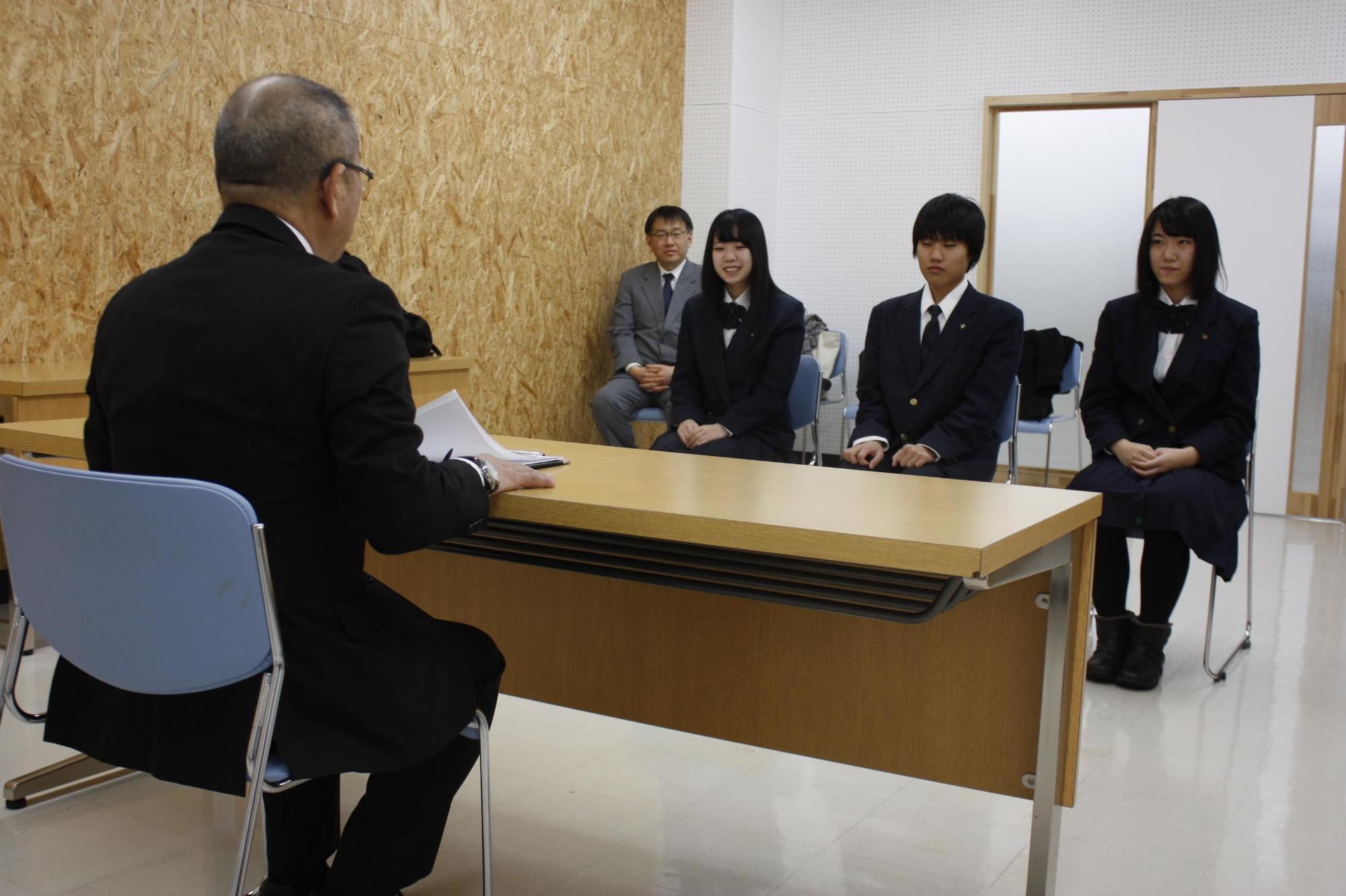 教育長と机を囲んで談笑する高校パソコン部の3人の部員の写真
