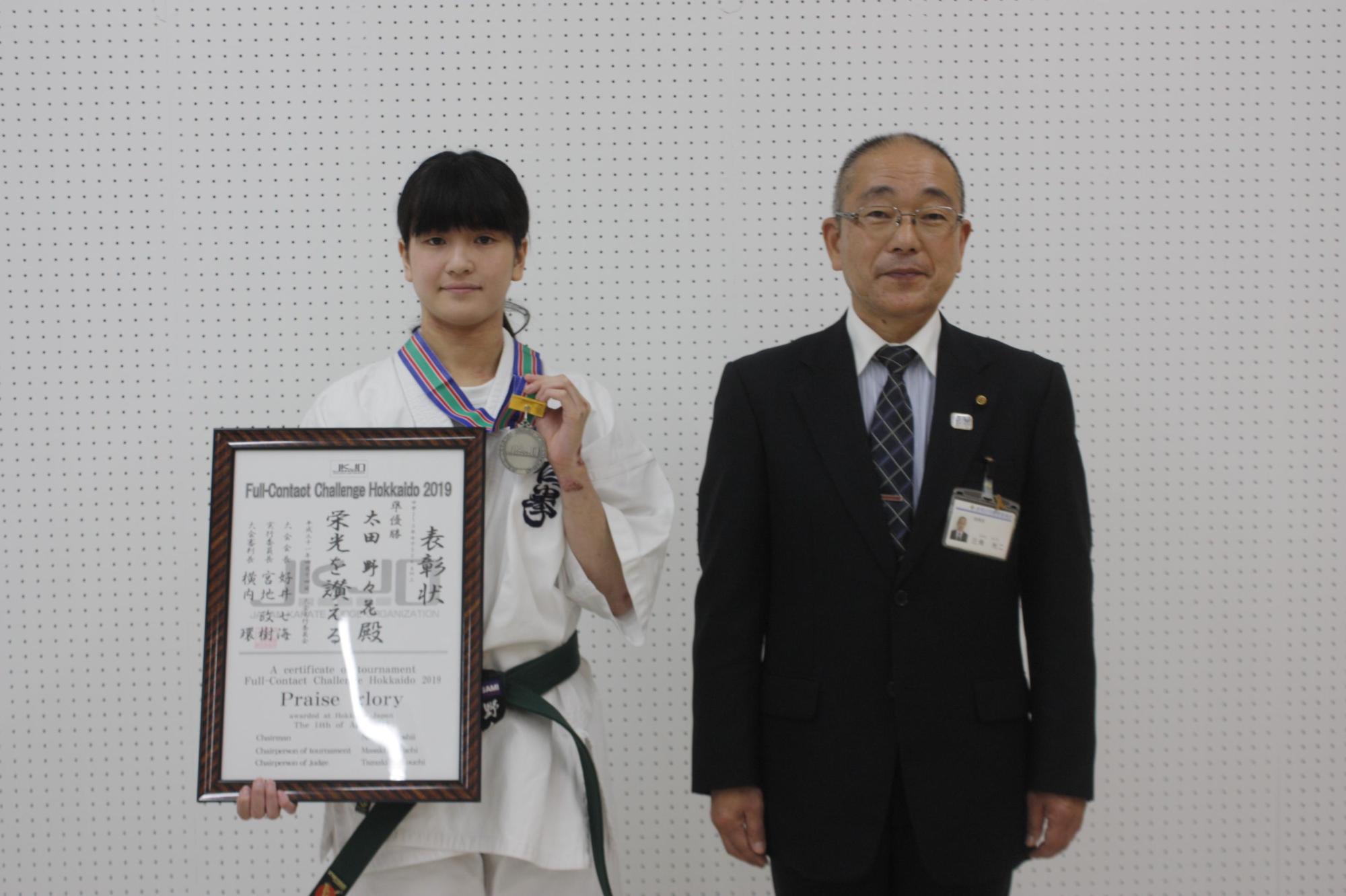 メダルをかけ、 右手に賞状を持っている太田さんと教育長が並んでの記念撮影の写真