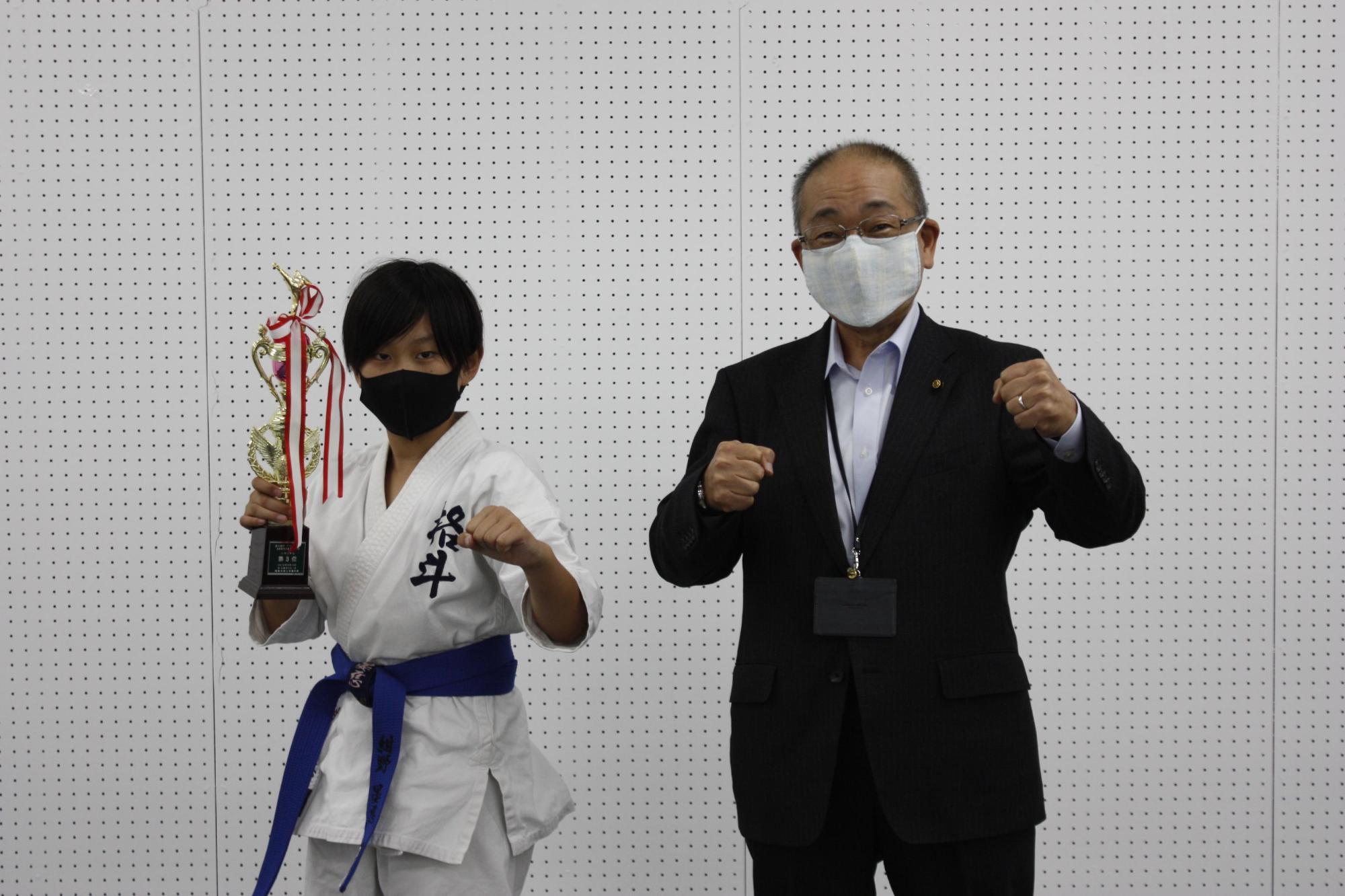 右手にトロフィーを持って構えている紺野さんと教育長が並んでの記念撮影の写真