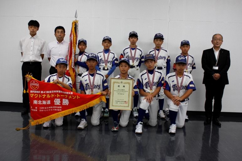 教育長と優勝旗を持った岩見沢南ビクトリーの皆さんの集合写真