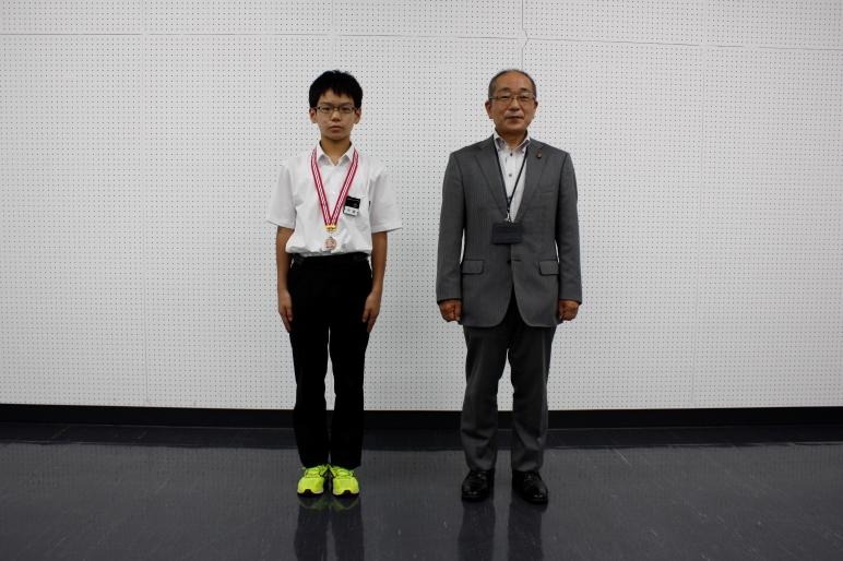 教育長と首にメダルをかけた男子生徒と並んで撮影しる写真