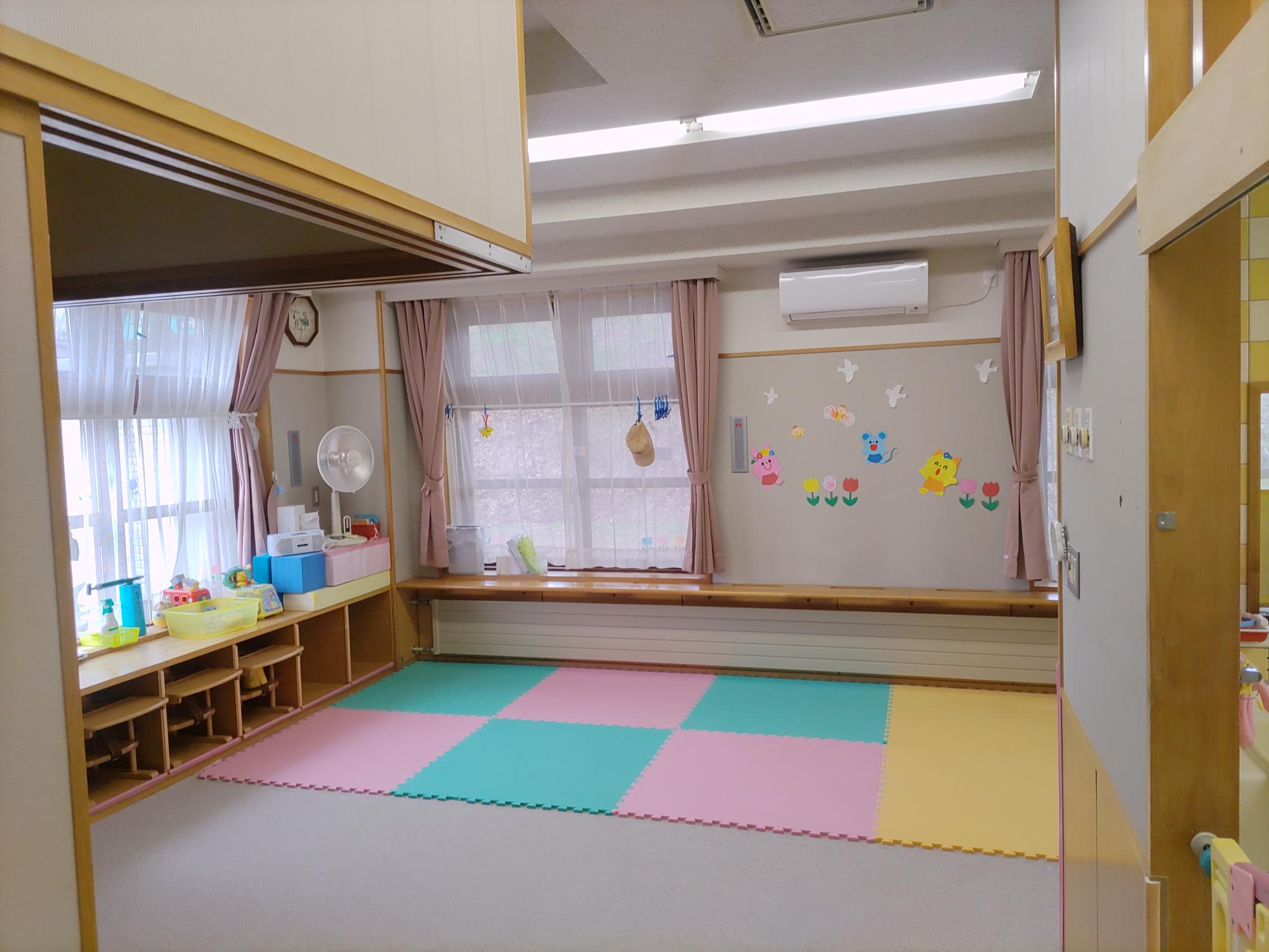 白いカーペットに色とりどりのマットを敷いてある未満児（0歳児）保育室