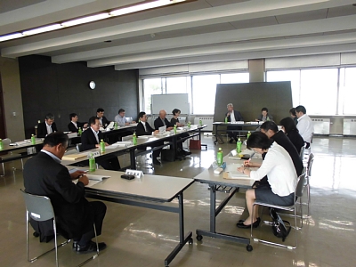 大きな窓のある会議室内で、四角形に並べられた机の前の椅子に座りながら会議に参加する人々の写真