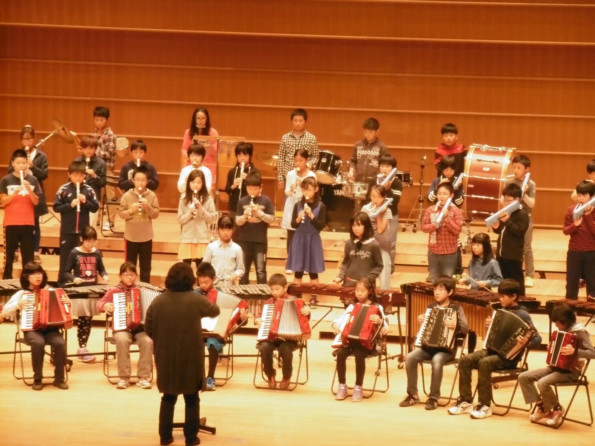 子供たちがアコーデオンやリコーダーなどを舞台上で演奏している写真