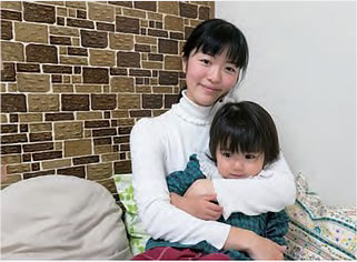 子どもを抱きかかえ笑顔で座っている嘉屋亜湖さんの写真