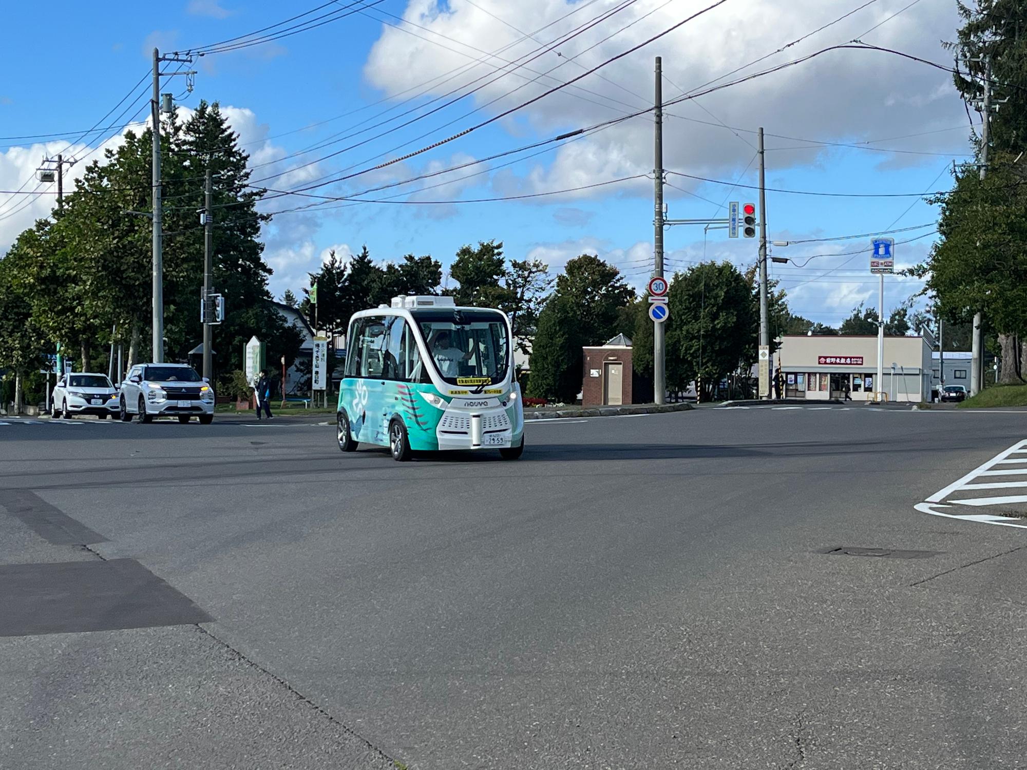公道の交差点内を走行しているラッピングされた自動運転EVバスの写真