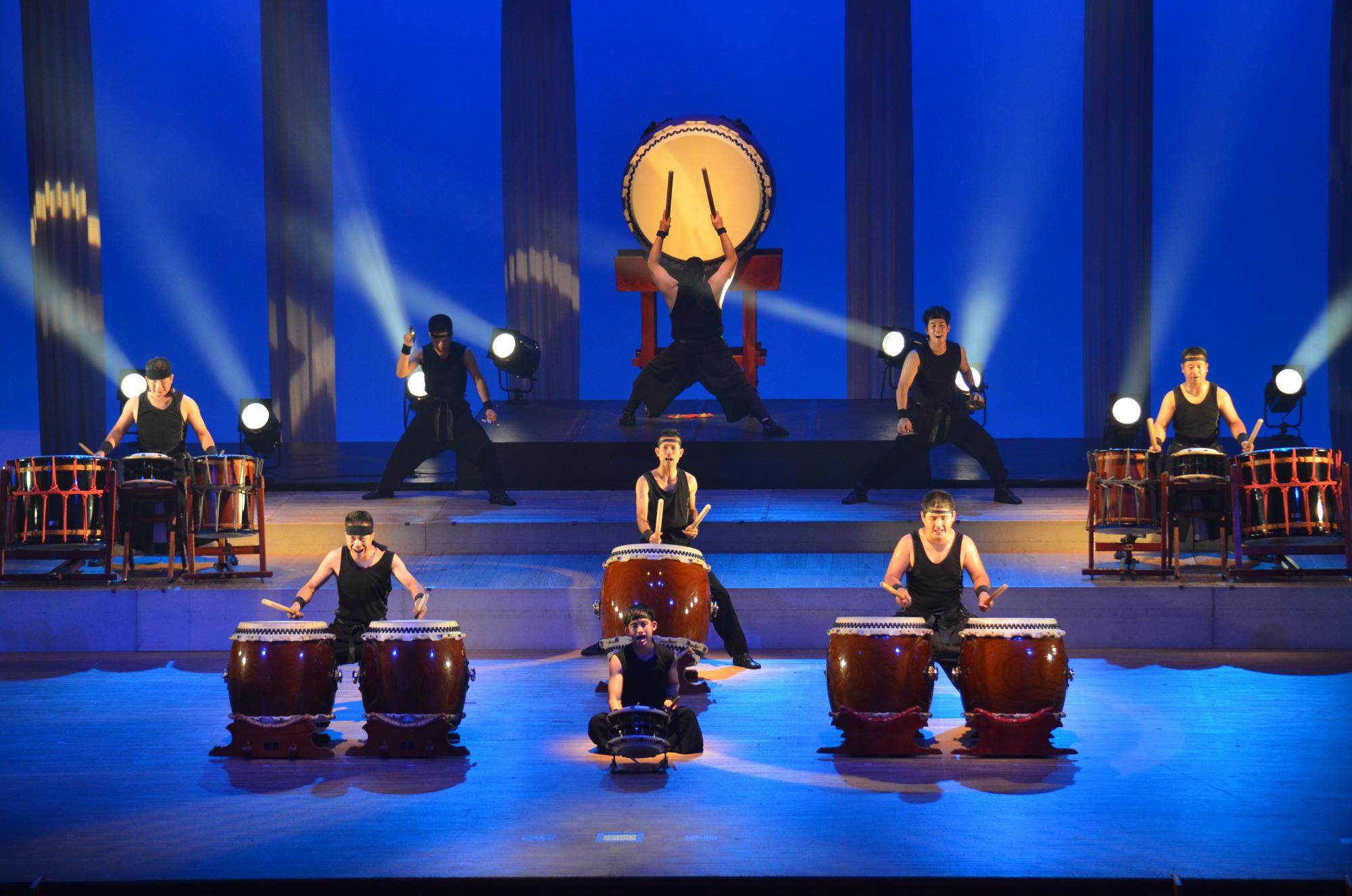 青い背景に黄色い光を透かす大太鼓を中央に置いた月夜をイメージした和太鼓演奏の写真