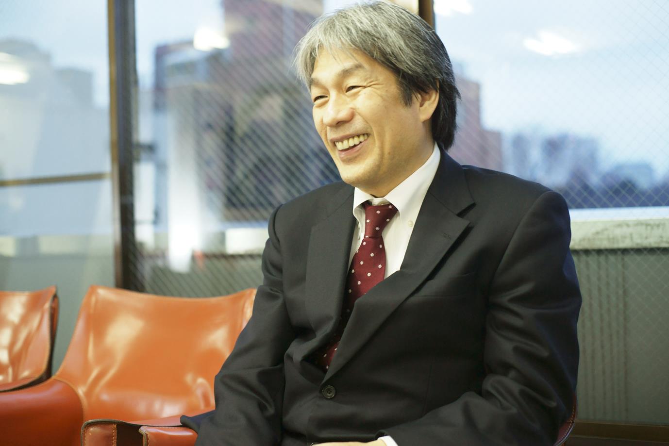 笑顔でインタビューに応えるスーツ姿の野澤和弘さんの写真