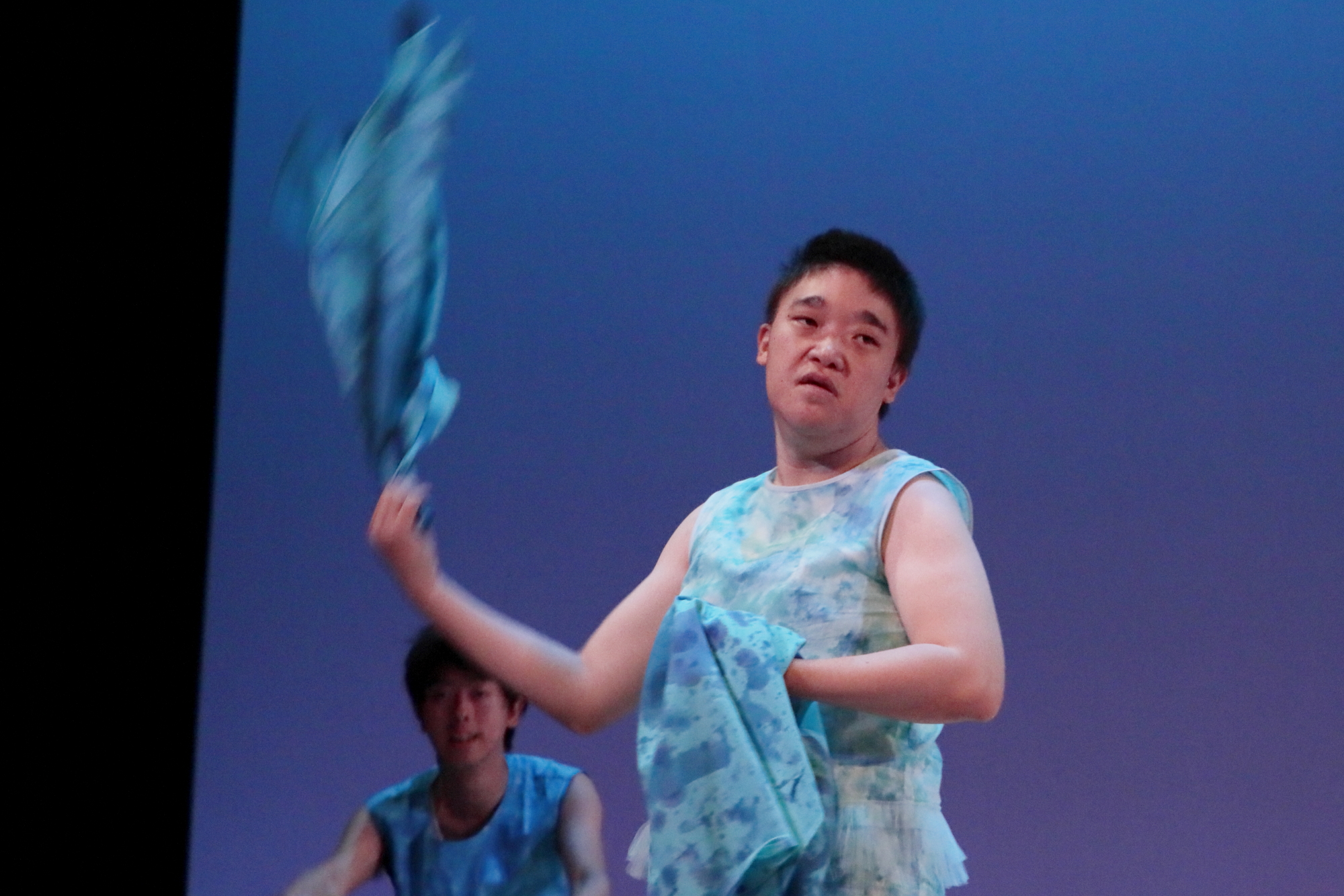 舞台の上で青い絞り染めの布を力いっぱいに振り回す男性の写真
