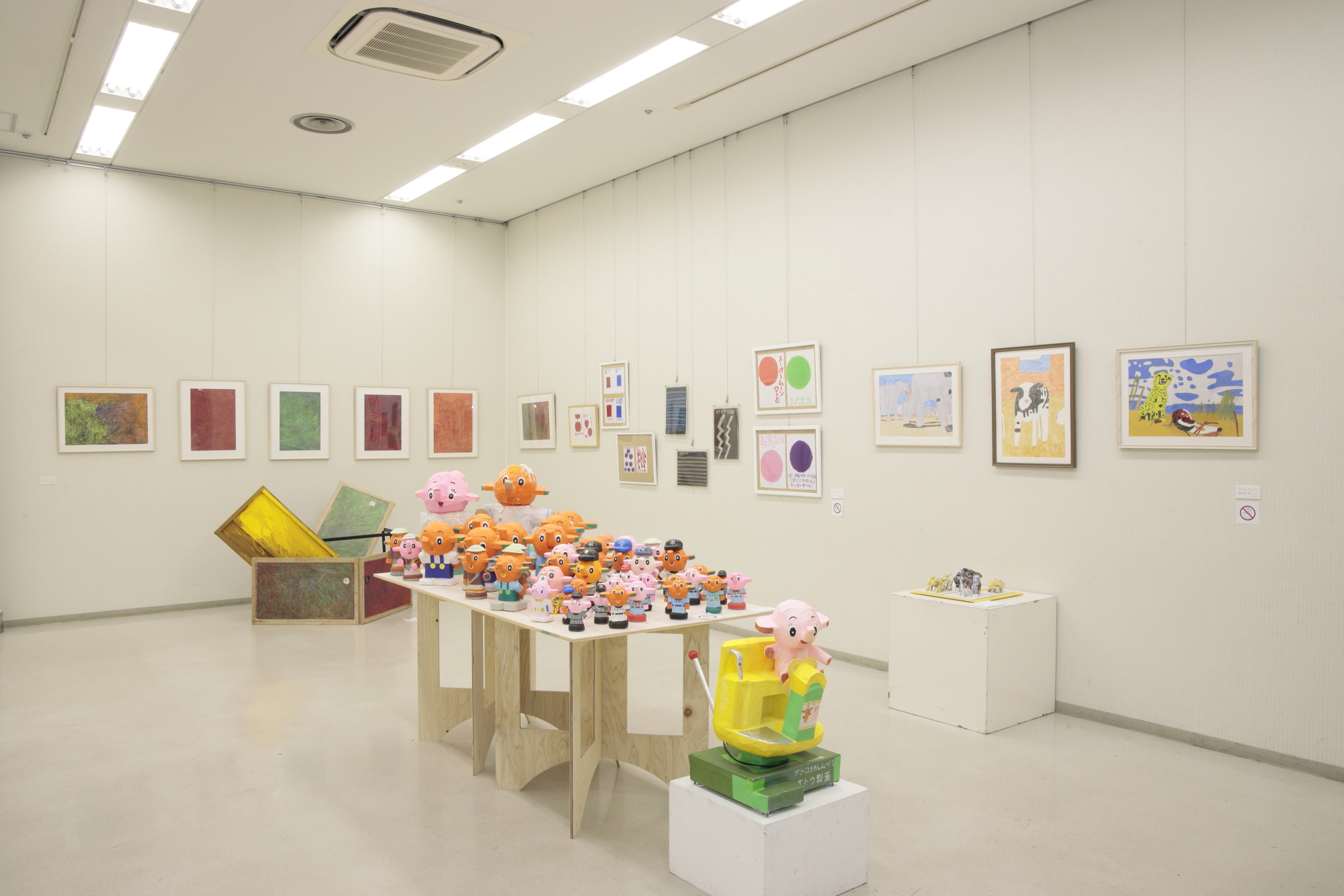 室内の白い壁に飾られた絵画や、中央のテーブルに色とりどりの象のキャラクターが置かれた展示会の写真