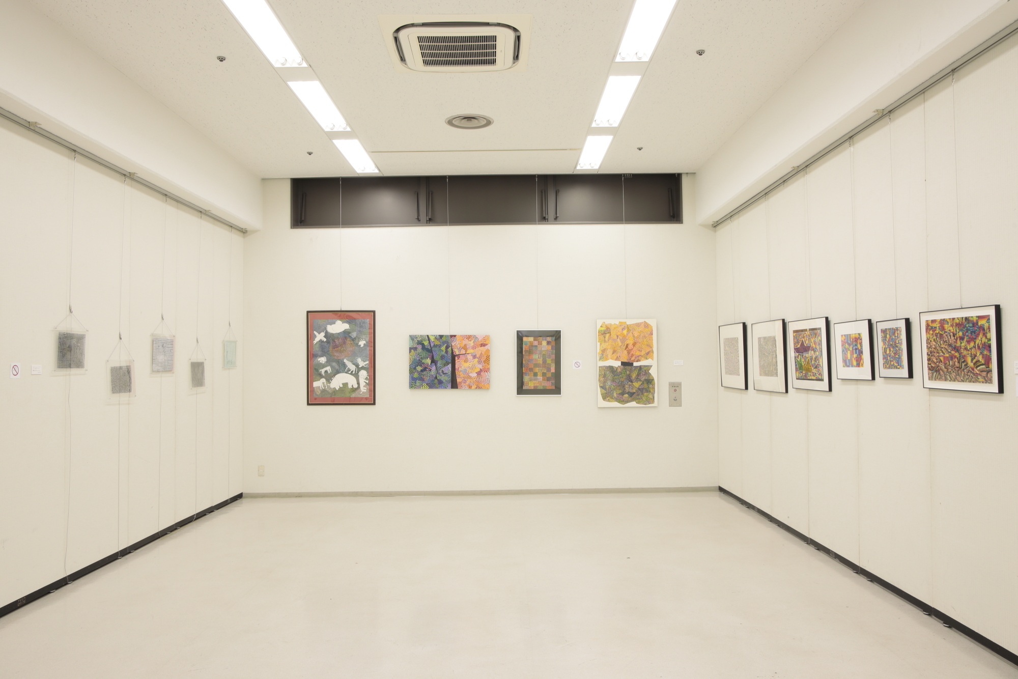 室内の白い壁に何枚もの絵画が整然と飾られた展示会の写真