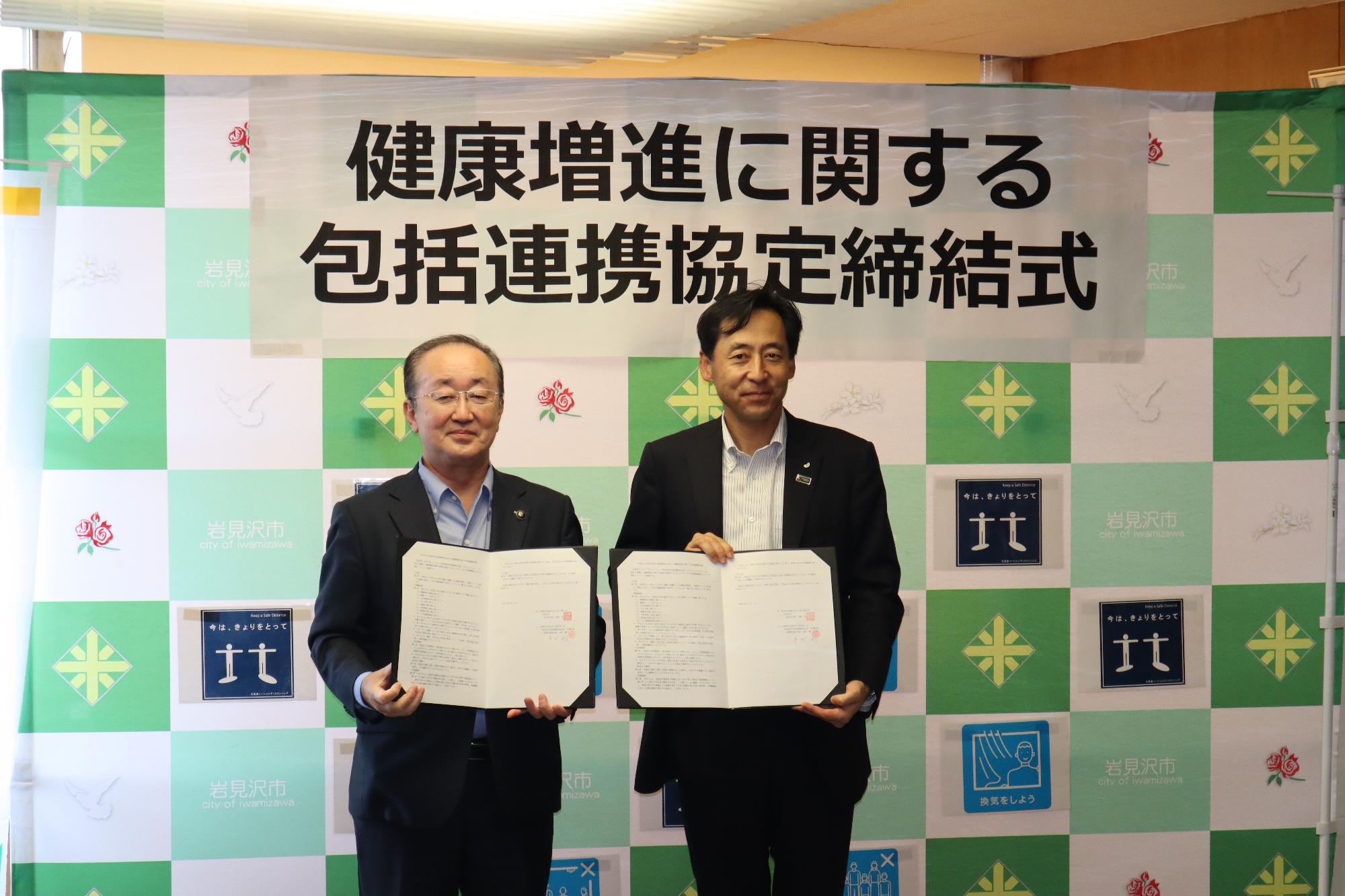 松野市長と本村支社長が署名した協定書を持ってバックボードの前で記念撮影