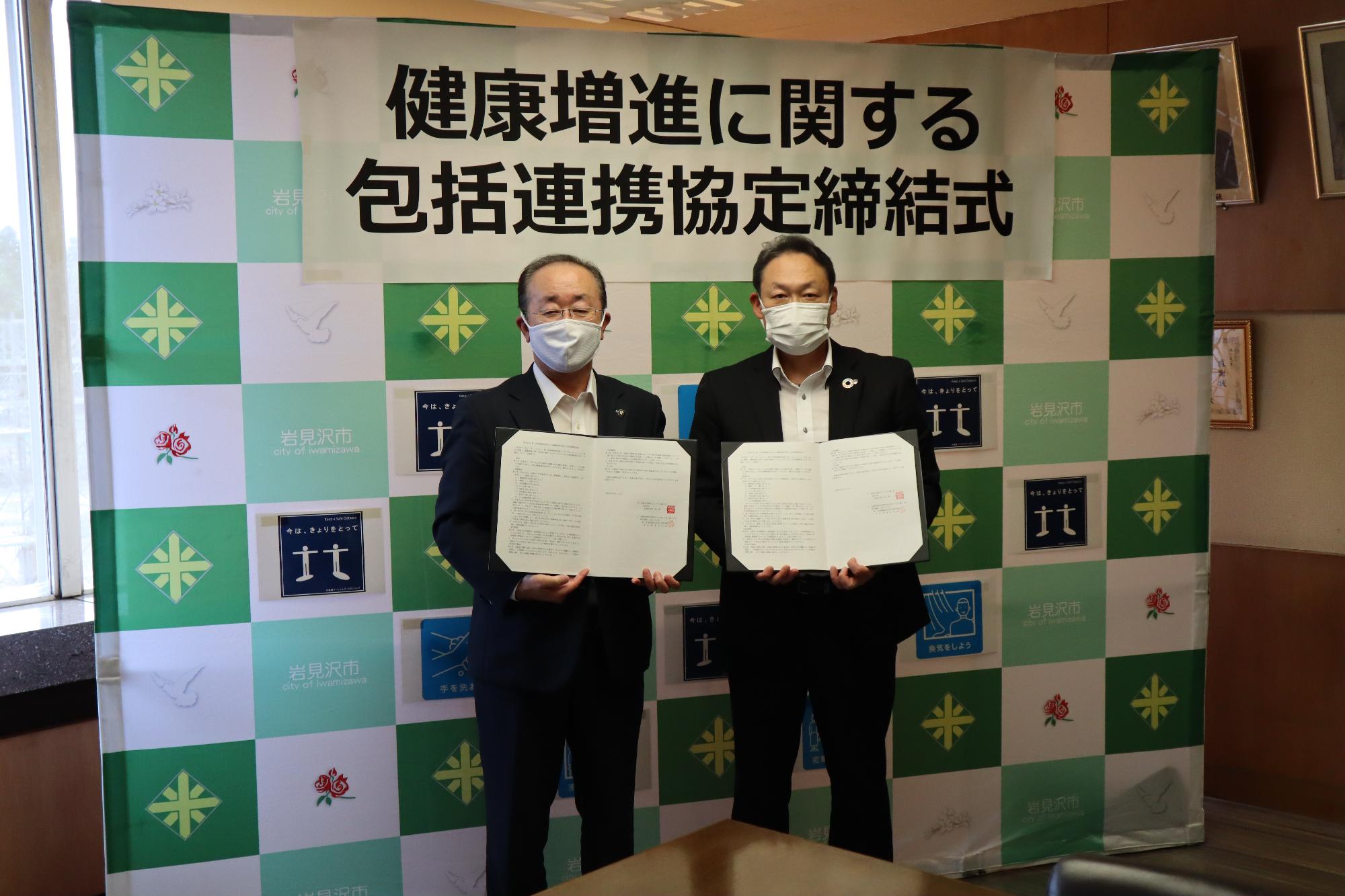 松野市長と深谷支社長が署名した協定書を持ってバックボードの前で記念撮影