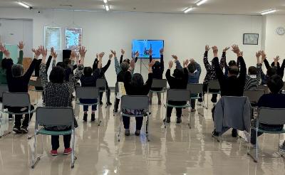 椅子に座りながら両手を高く上げている介護予防体操の様子