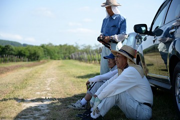 ブドウ畑で男性2人が座り、男性1人が立って休憩している様子の写真