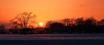 雪原の奥に夕日が沈んでいく様子の写真