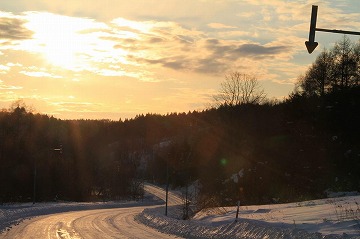 手前から奥にS字の雪道と夕日が写っている写真