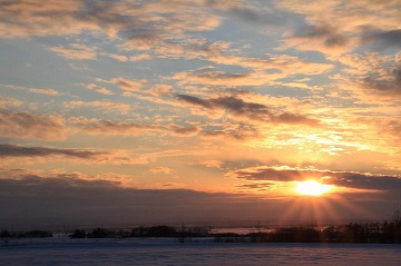 雪原と雲がかかっている夕日が沈んでいる様子の写真