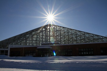 三角屋根の建物と太陽が写っている雪景色の写真