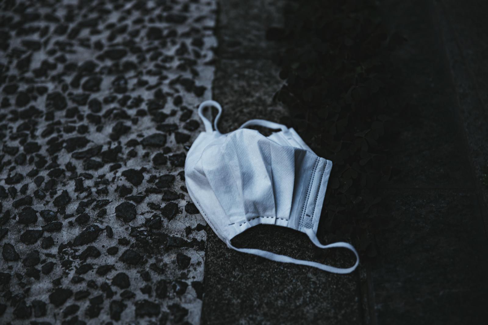 コンクリートの路上にポイ捨てされた白いマスクの写真