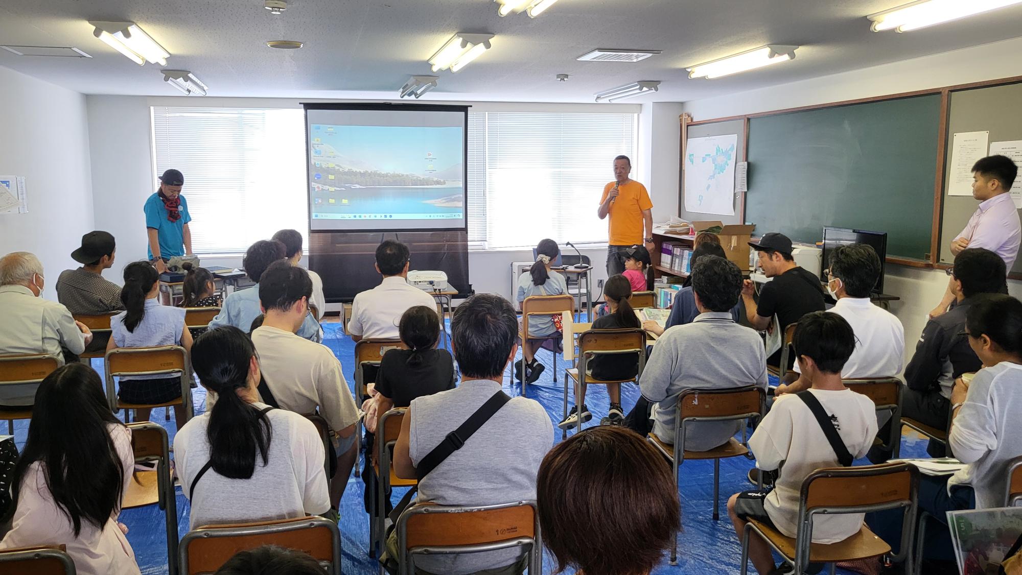 特殊塗装「ポリウレア」の紹介をする株式会社高橋工務店の工藤社長と参加者の写真