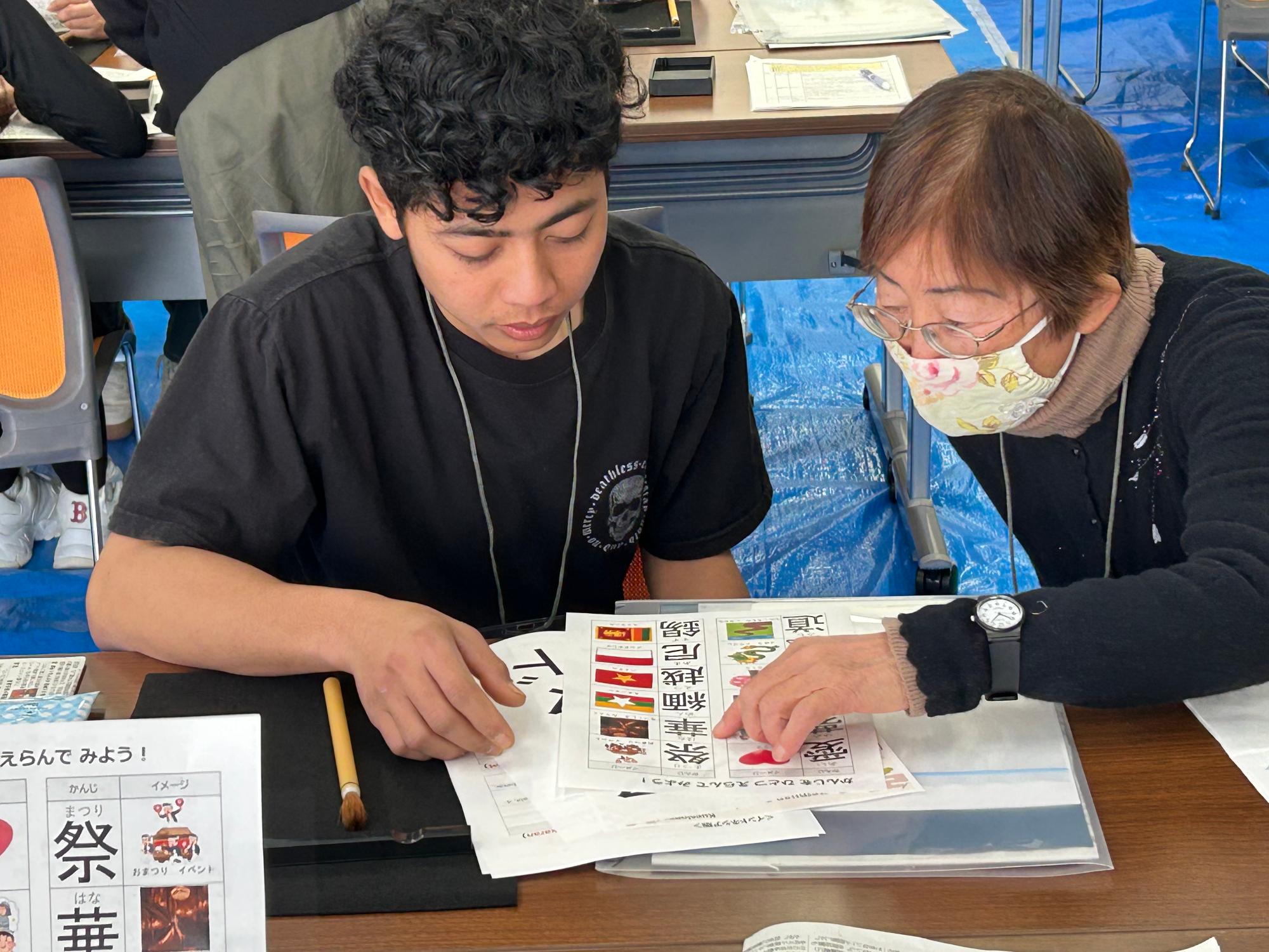 外国人の方と日本人のボランティアの方が書道で書く漢字を選んでいる様子