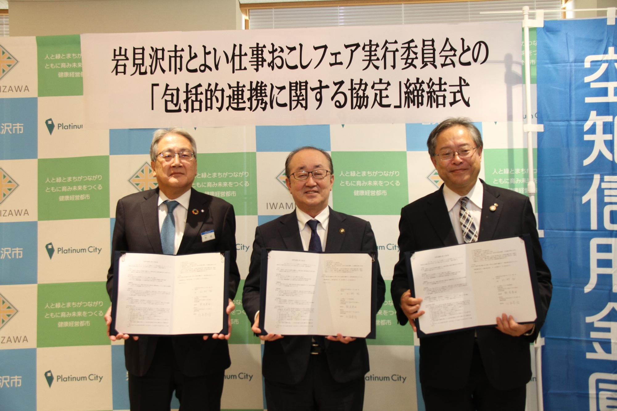 空知信用金庫の熊尾理事長、岩見沢市の松野市長、城南信用金庫の川本理事長が協定書を持ち、並んで立っている画像