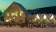 空が薄暗くなり、室内から照明の灯りがみえる、ロッジの外観写真。ロッジのまわりは雪で白く、大勢のスキー客の姿がみえる。