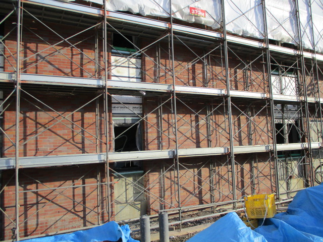赤レンガの外壁に工事の足場が設けられている様子を左斜め前から写した写真。