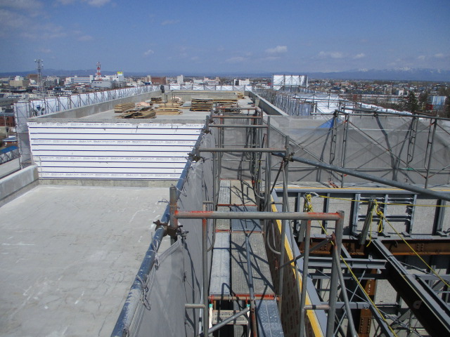 屋上の工事現場を撮影した写真。大空の下、屋上一面に工事の様子が写っている。