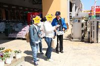 青いハッピを着た男性が選挙啓発物品を中央の女性に渡している様子の写真