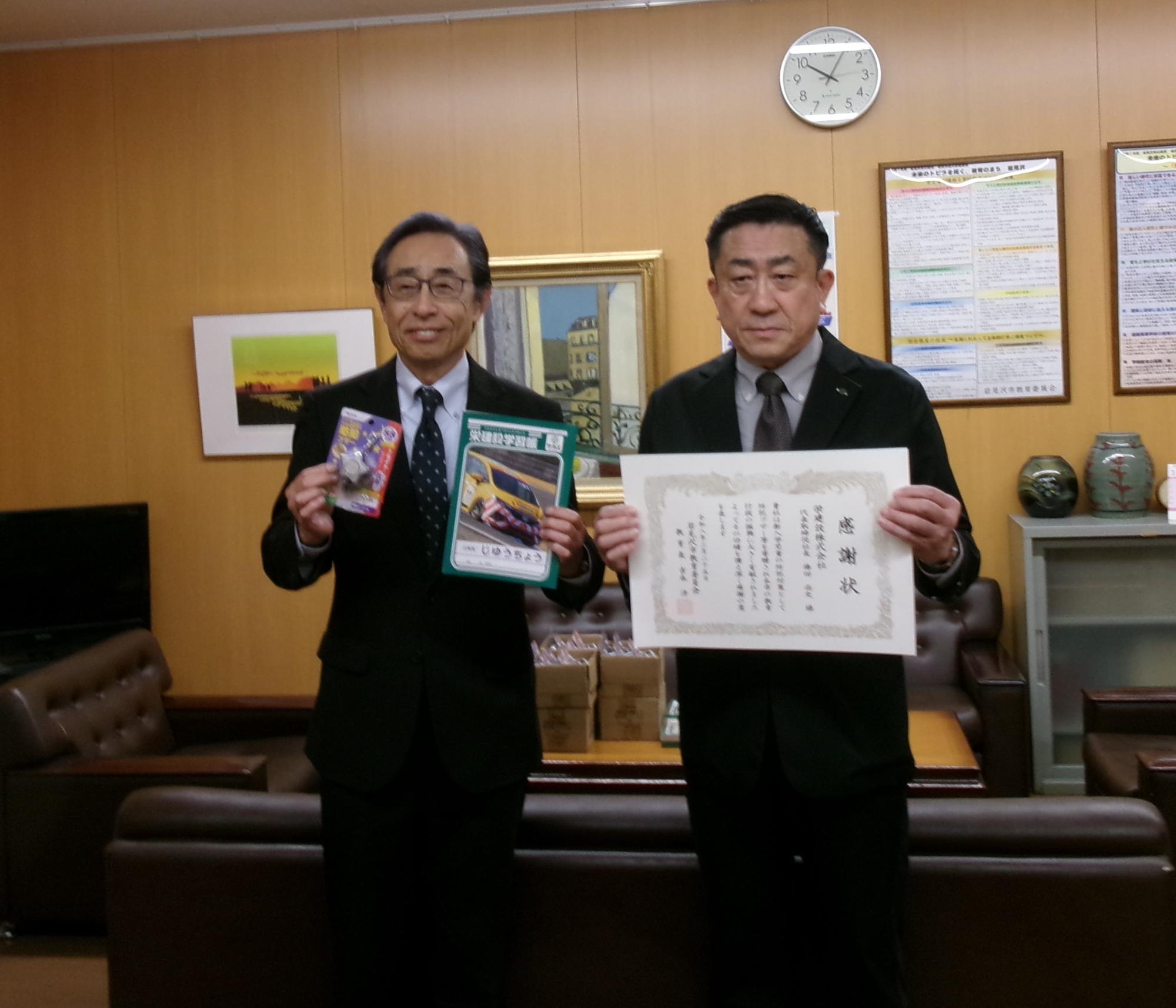 教育長が栄建設株式会社様から防犯ブザーと学習帳を受け取り、栄建設株式会社様へ教育長より感謝状を贈呈しています。