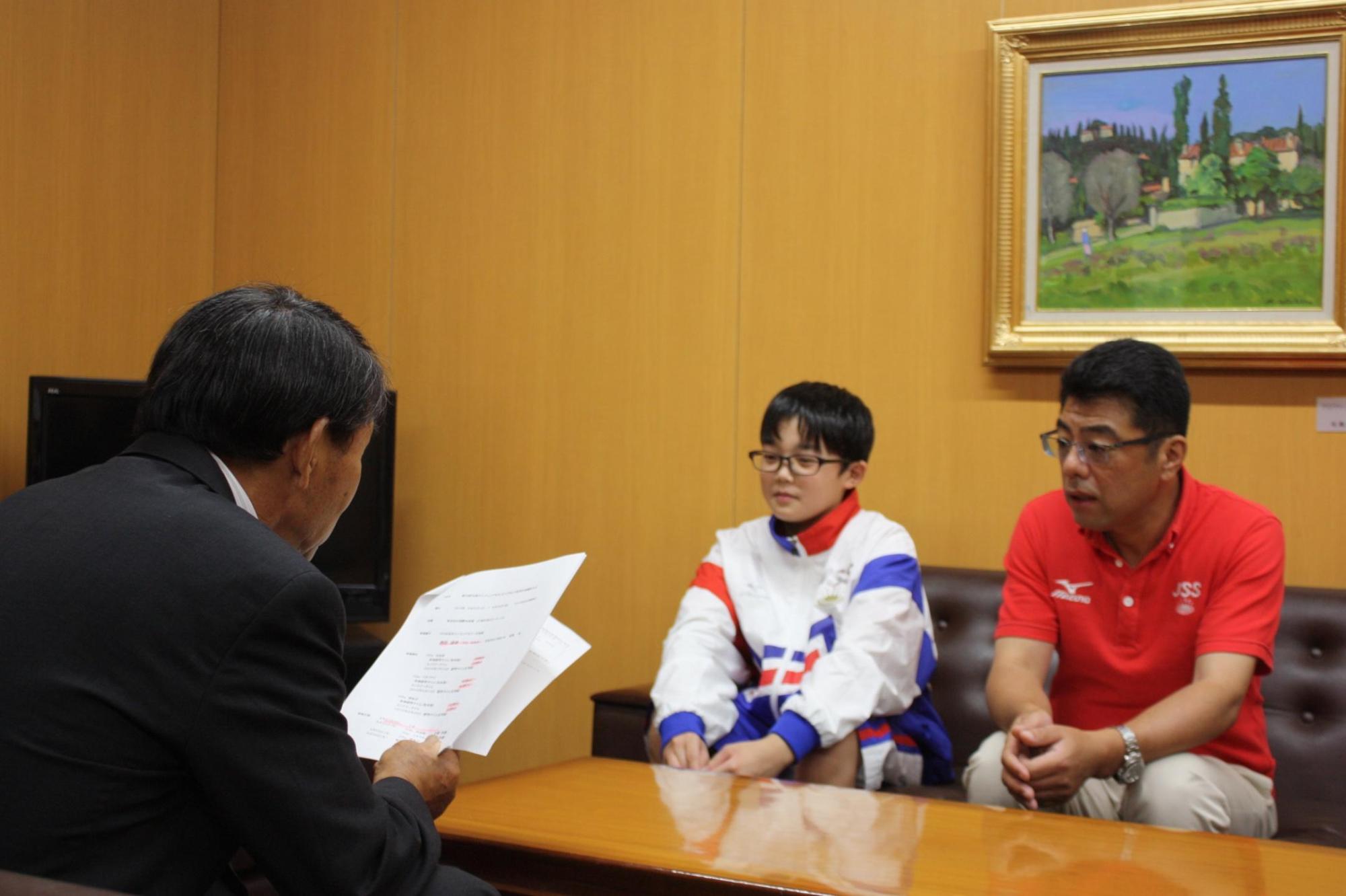 諏訪さんとコーチと並び教育長の話を聞く写真