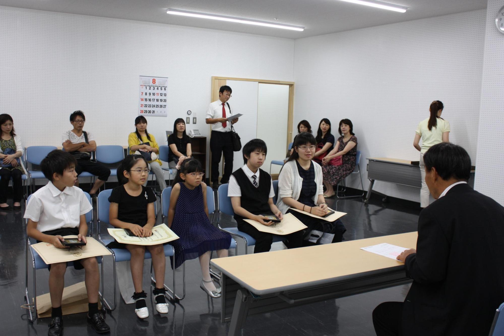 机を挟み症状を持った上位入賞者のみなさんが教育長の話を聞いている写真