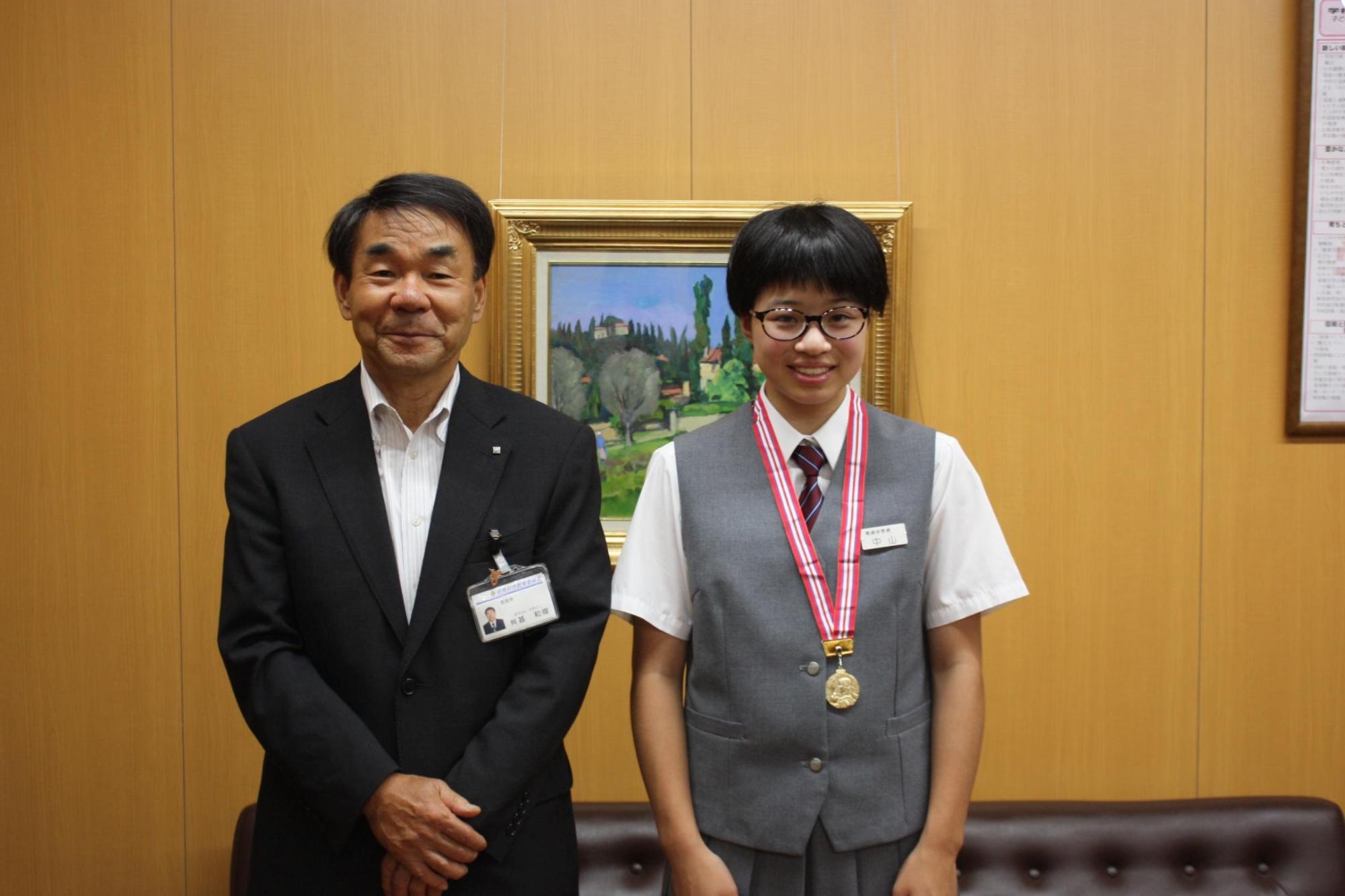 金メダルを下げた中山さんと並ぶ教育長の写真