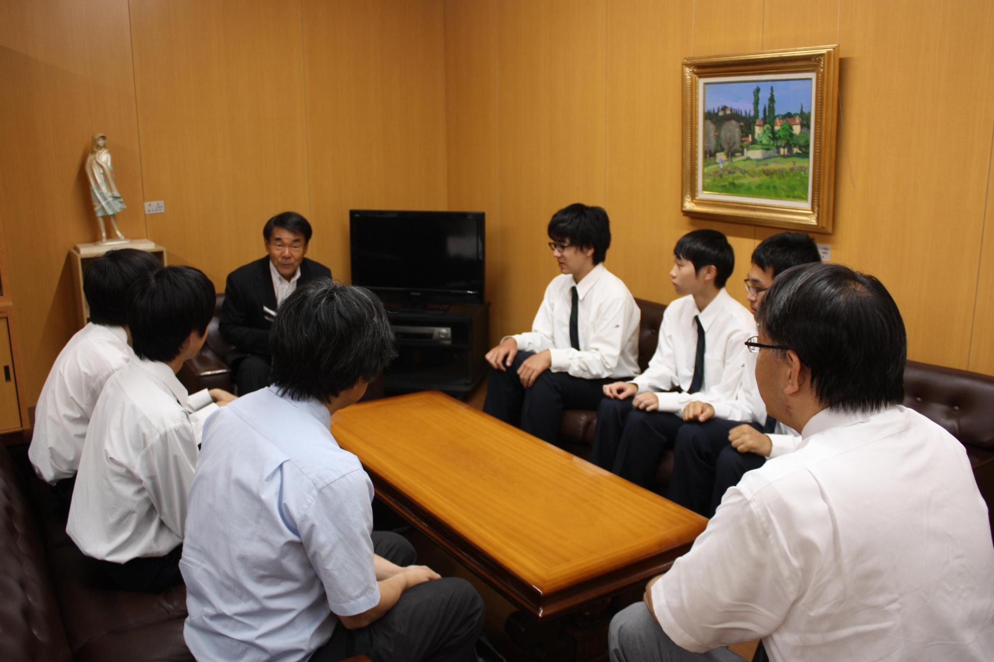 机を囲み上座に座る教育長の話を聞く荻野さん、阿部さん、簿記部の皆さんの写真