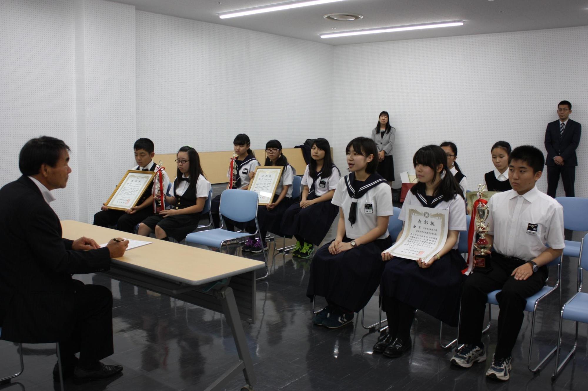 机を挟み教育長の話を吹奏楽部の皆さんが効いている様子の写真