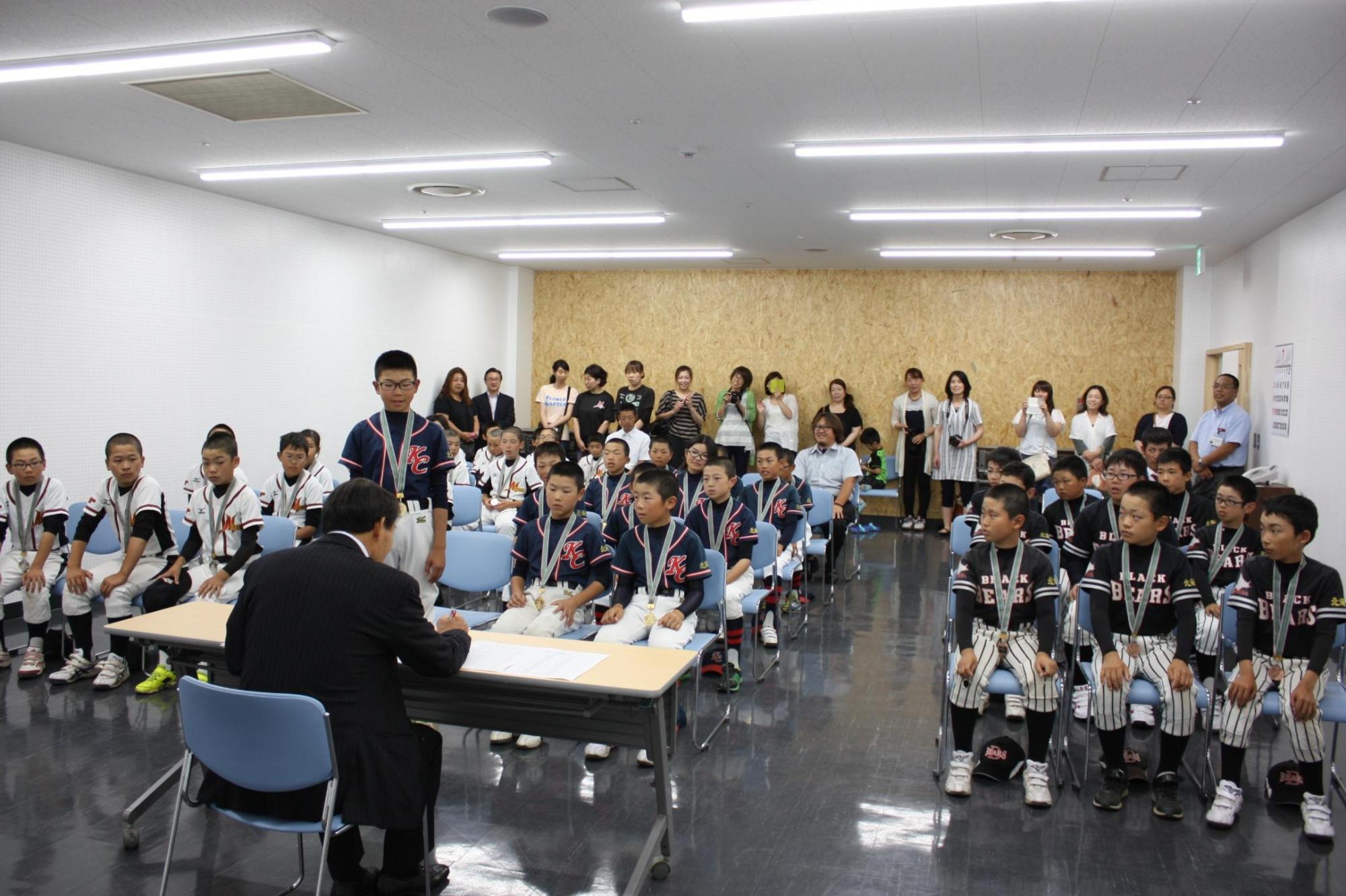 広い部屋で栗沢コンバット 岩見沢東ブラックベアーズ 岩見沢美園スターズの皆さんが教育長と向かいあって座っている様子の写真