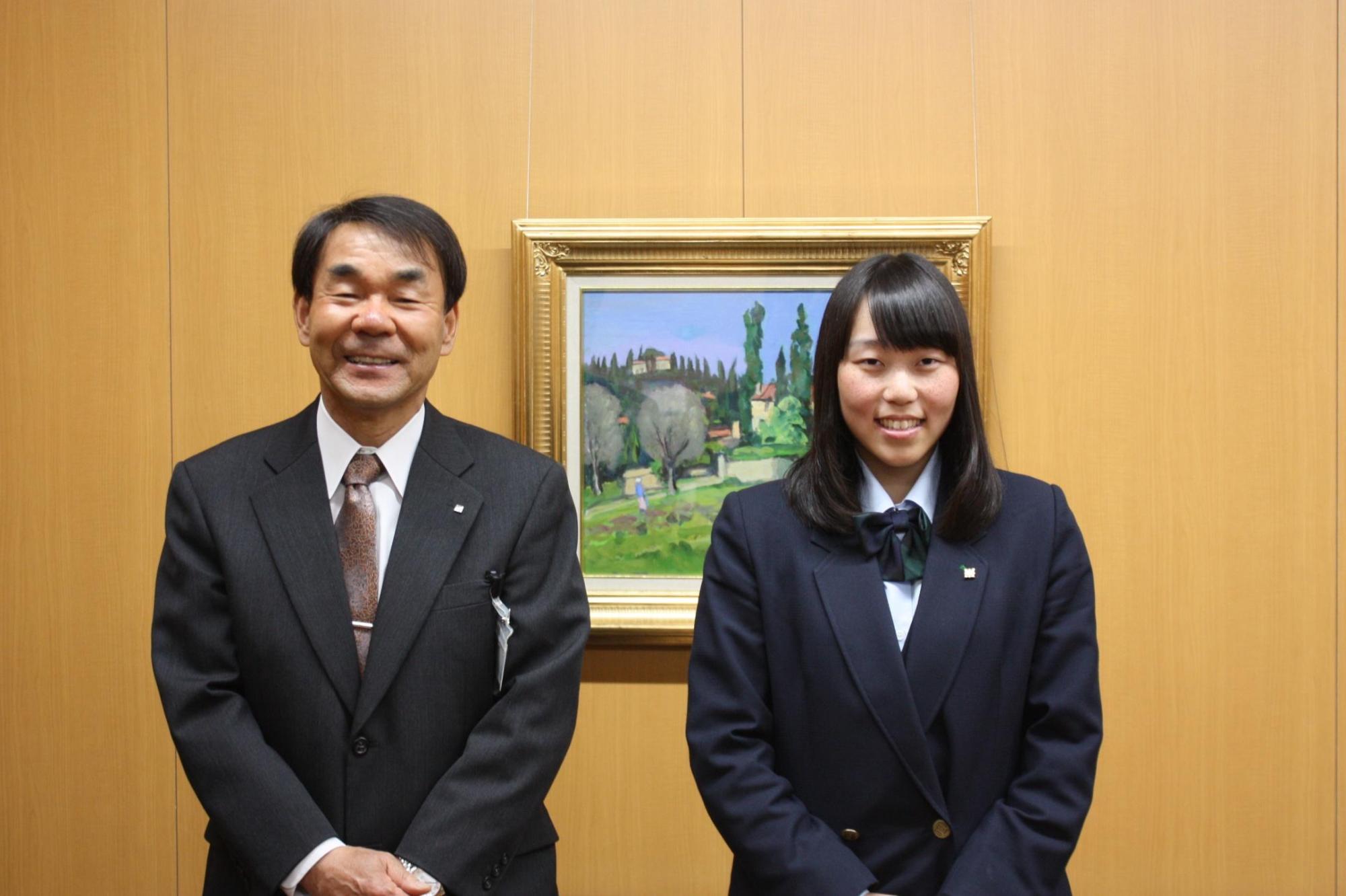 教育長と加藤彩音さんと撮影した写真。二人とも正面を向いて笑顔で撮影にのぞんでいる。