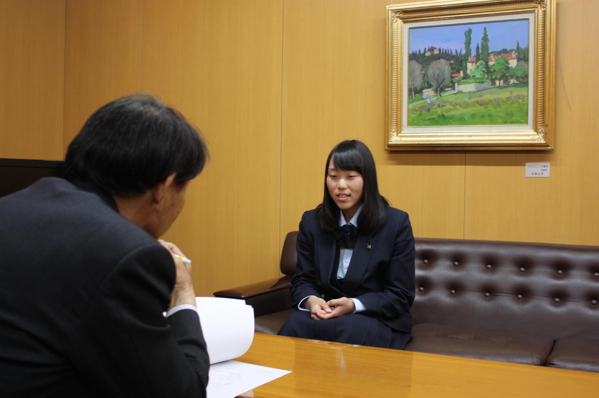 教育長と加藤彩音さんと撮影した写真。二人ともソファに腰かけ、机を挟んで話をしている。
